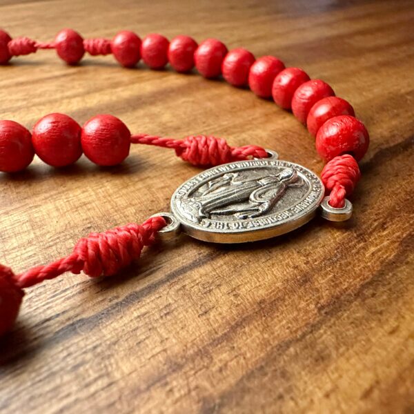 Ein roter Rosenkranz liegt auf einen dunklen Holztisch - die wuntertätige Medaille ist im Mittelpunkt