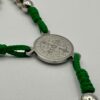 Rosenkranz mit 6mm Metallperlen und grüner Kordel liegt auf weisen Hintergrund - Nahaufnahme der Benediktusmedaille