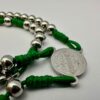 Rosenkranz mit 6mm Metallperlen und grüner Kordel liegt auf weisen Hintergrund - Nahaufnahme der Benediktusmedaille und einigen Perlen