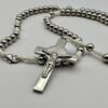 Rosenkranz mit 6mm Metallperlen und weisser Kordel liegt auf weissen Hintergrund - man sieht das Kreuz und einen Teil des Rosenkranzes