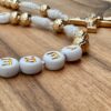 Man sieht einige Buchstabenperlen und ein goldenes Kreuz eines personalisierten Rosenkranzes