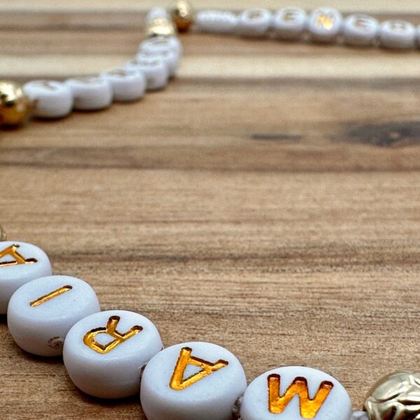 Man sieht einige Buchstabenperlen eines goldenen personalisierten Rosenkranzes