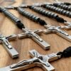 einige offene 10er Rosenkränze mit Hämatitperlen und Benediktuskreuzen liegen auf einem dunklen Holzuntergrund