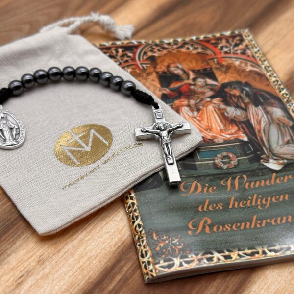 10er Rosenkranz liegt auf Baumwollbeutel und einem Rosenkranz-Gebetsheft