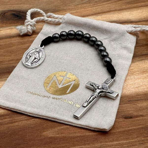 Man sieht einen 10er Rosenkranz mit Hämatit-Perlen der auf einem Bauwollbeutel liegt