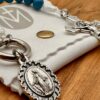 Verzierte wundertätige Medaille eines 10er Rosenkranzes als Schlüsselanhänger auf einem weißen Täschchen