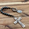 Hämatit-Rosenkranz mit 10 Perlen, einem Kreuz mit der Dreifaltigkeit und einer wundertätigen Medaille - der Rosenkranz liegt offen auf dunklen Holz