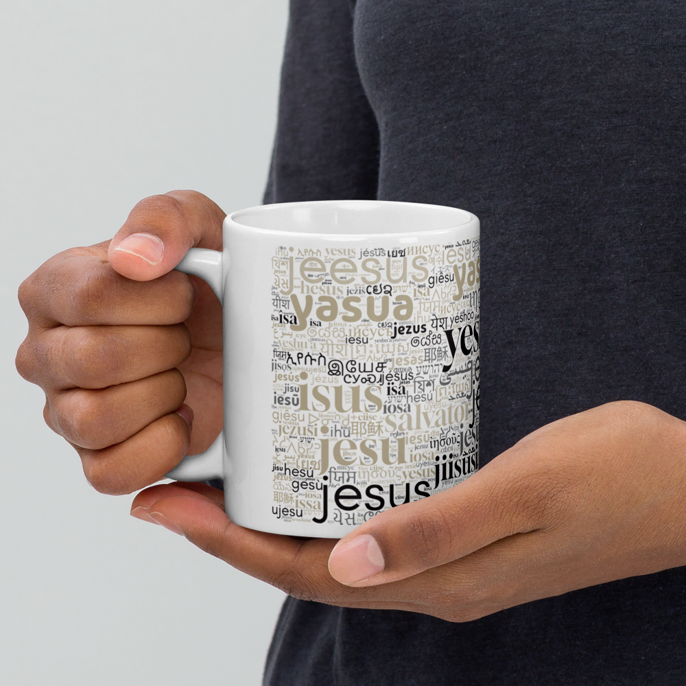 Eine Mann hält eine weiße Tasse mit dem Namen Jesus in vielen verschiedenen Sprachen in den Händen - der Henkel wird in der rechten Hand gehalten.