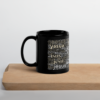 Schwarze Tasse mit dem Namen Jesus in allen Sprachen der Welt auf einem Holzbrett mit dem Henkel nach links