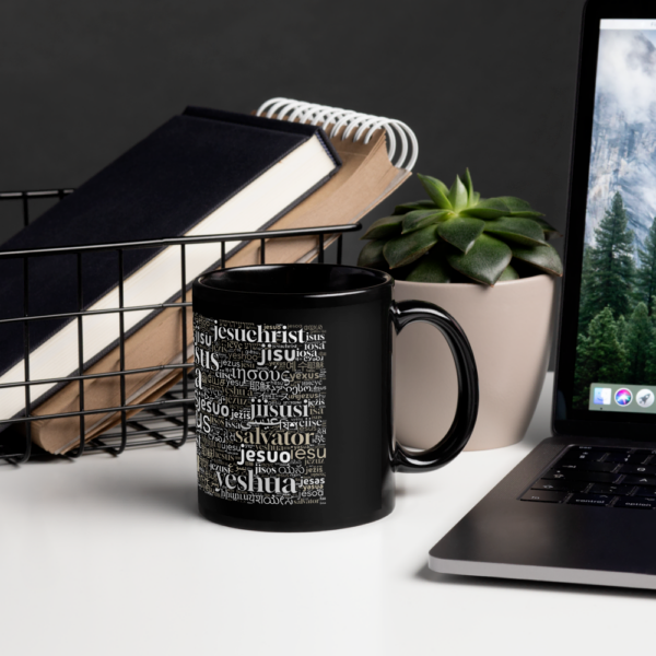 Schwarze Tasse mit dem Namen Jesus in vielen Sprachen steht neben einem Laptop