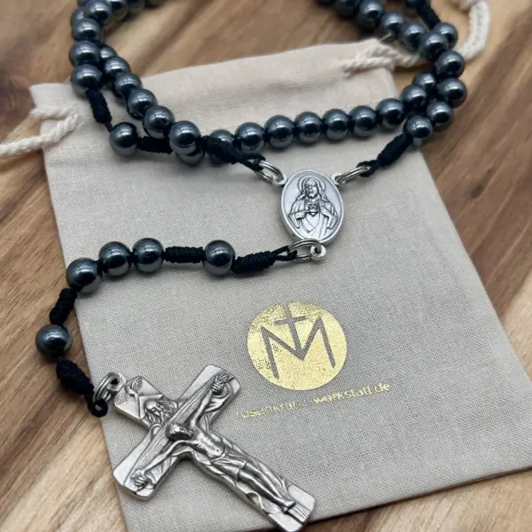 Rosenkranz Gottes Liebe aus Hämatit-Perlen mit silbernem Herz-Jesu-Mittelstück und Kruzifix auf Geschenkbeutel