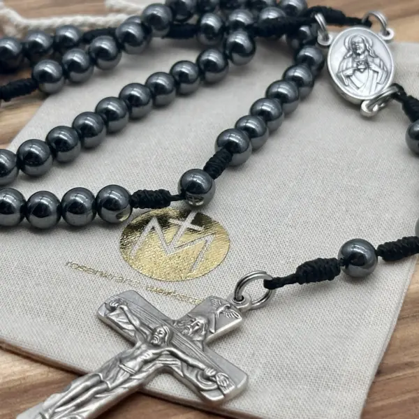 Rosenkranz aus Hämatit mit silbernem Kruzifix auf beigem Stoff-Geschenkbeutel der Rosenkranz Werkstatt