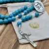 Benediktuskreuz des türkisfarbenen Medjugorje-Rosenkranzes auf dem Geschenkbeutel