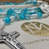 Schönstatt-Kreuz und türkise Glasperlen auf dem Geschenkbeutel der Rosenkranz Werkstatt