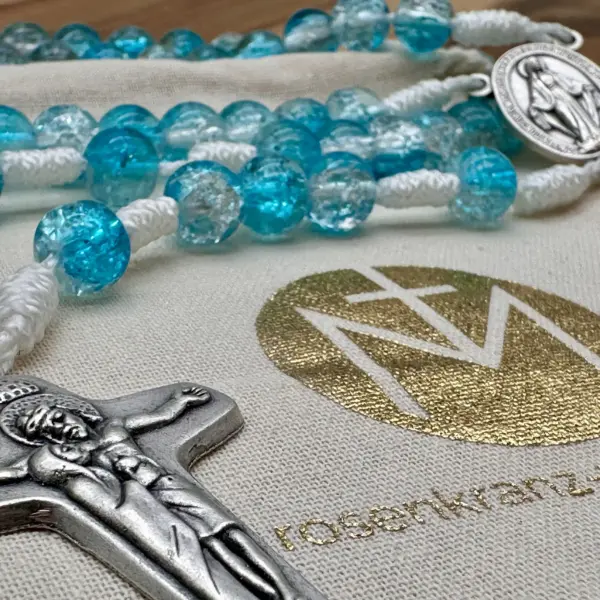 Schönstatt-Kreuz und türkise Glasperlen auf dem Geschenkbeutel der Rosenkranz Werkstatt