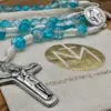 Silberfarbenes Schönstatt-Kreuz des türkisen Rosenkranzes auf dem Geschenkbeutel
