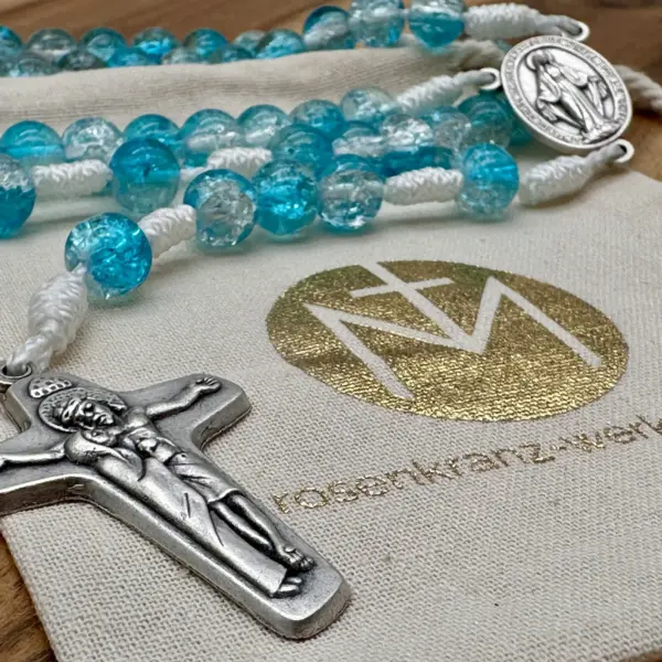 Silberfarbenes Schönstatt-Kreuz des türkisen Rosenkranzes auf dem Geschenkbeutel